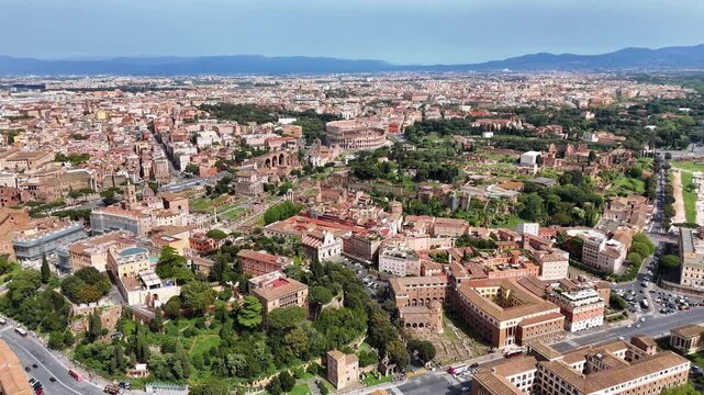 Aerial drone view of Rome's historic center featuring the Colosseum, Roman Forum, and Palatine Hill. Ancient ruins surrounded by modern cityscape under clear daylight