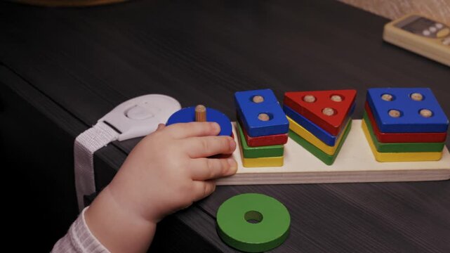 Toddler hand reaches for and grabs a colorful wooden shape sorter toy. Close-up shot captures the child fine motor skill development during playtime.
