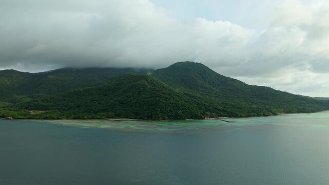 Aerial view of the Turtle Conservation, where lush green mountains meet the turquoise sea under a cloudy sky, Karimunjawa National Park, Karimunjawa, Central Java, Indonesia.