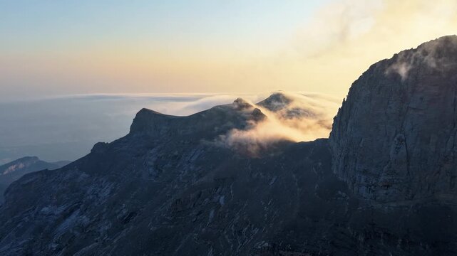 Aerial view of dramatic mountain peaks piercing through ethereal clouds, creating a stunning contrast of light and shadow, Mount Olympus, Larissa, Greece.