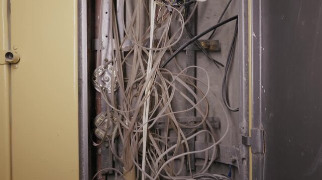 Chaotic mass of old electrical and telecommunication wires fills an open metal utility box. Camera tilts up revealing dusty cables, rusty connectors, and neglected maintenance infrastructure.