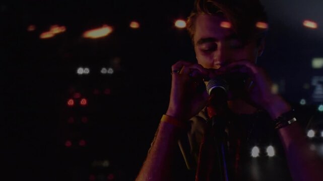 Animation on blurred night road traffic over caucasian man playing harmonica on concert