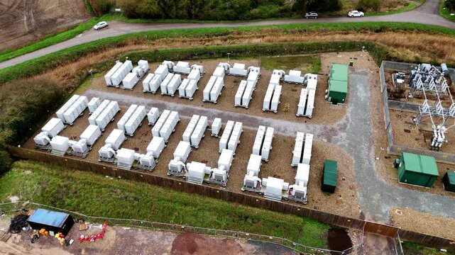 Aerial view of rows of white battery energy storage systems contrasting against green grass near an electrical substation, Burwell, Burwell, United Kingdom.