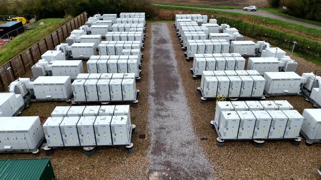 Aerial view of rows of battery energy storage systems stand in organized arrays on gravel ground, Burwell, United Kingdom.