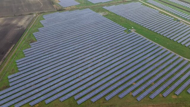 Aerial view of neat rows of solar panels, reflecting the sky, contrasting with the green fields, Burwell, England, United Kingdom.