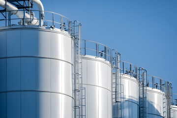 Row of Shiny White Industrial Storage Tanks under Blue Sky