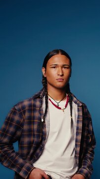 Confident young man with braids posing in a studio portrait against blue background