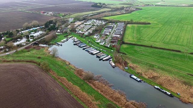 Aerial view of boats docked at Stretham Ferry Marina, nestled amongst verdant fields and quaint buildings, creating a picturesque scene, Ely, United Kingdom.
