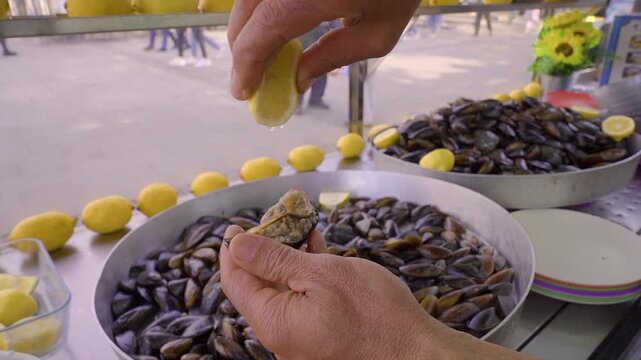 Hands squeezing fresh lemon on stuffed mussel at street food stall