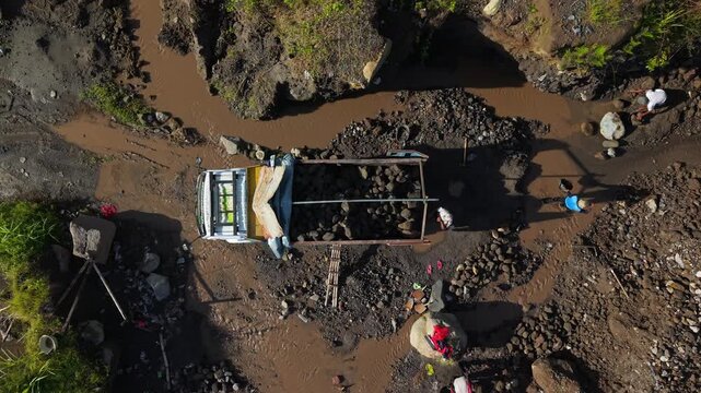 Aerial view of a truck in the muddy Woro River surrounded by rocks and greenery, creating a stark contrast, Klaten Regency, Central Java, Indonesia.