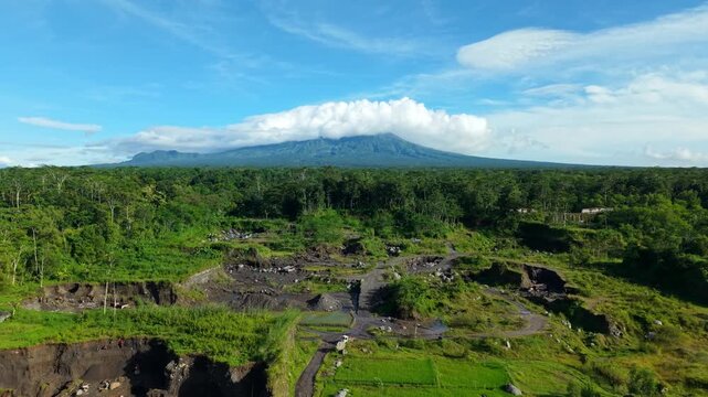 Aerial view of the stark contrast between the dark, rocky riverbed and the vibrant green rice paddies, Woro River, Klaten Regency, Central Java, Indonesia.