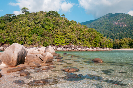 Rocky tropical coast with granite boulders in turquoise sea and lush rainforest hills at Tioman Island, Malaysia, natural island beach landscape.