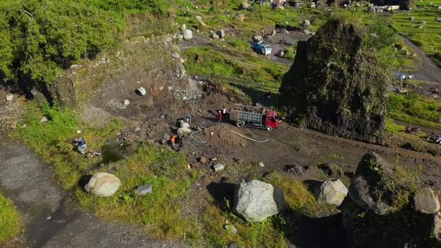 Aerial view of rocky terrain with a red truck and figures near Woro River, showcasing earthy tones against green vegetation, Klaten Regency, Central Java, Indonesia.