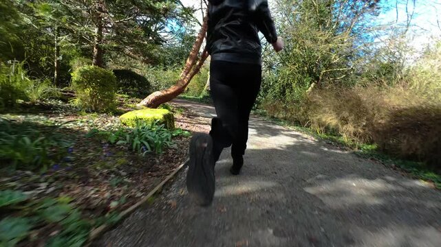 Running female legs on park path during escape from violent attacker. Low angle view of unrecognizable woman sprinting along garden trail creating crime thriller tension. Fast movement through green