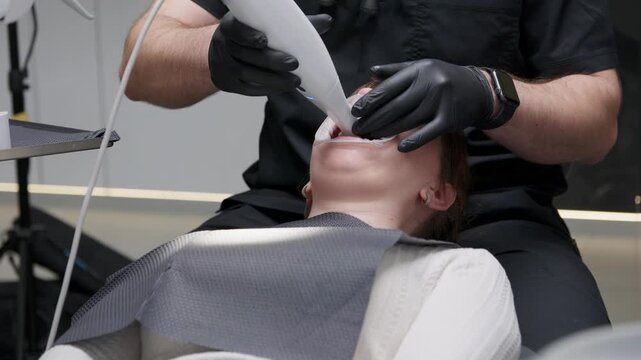 Professional orthodontist using an intraoral 3d scanner for dental scanning of a woman's teeth to create a digital impression during a consultation in a modern dental clinic