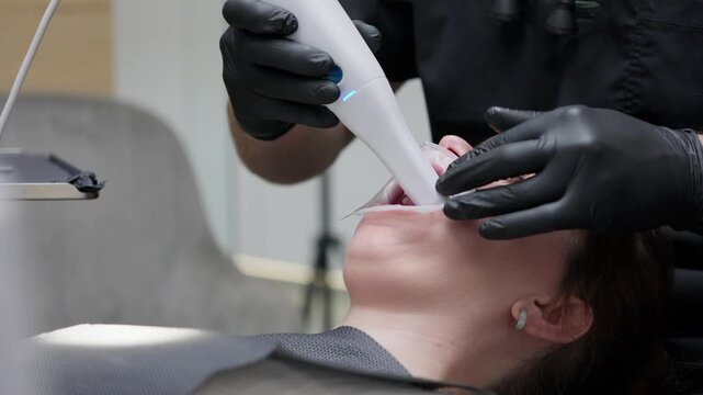 Professional orthodontist in black gloves using a modern 3d intraoral scanner for digital dental impressions while the patient is lying on a chair in the clinic during a checkup