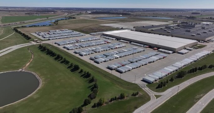Aerial view of a vast industrial complex with rows of trailers and a large building, set against a backdrop of green fields, Greensburg, Indiana, United States.