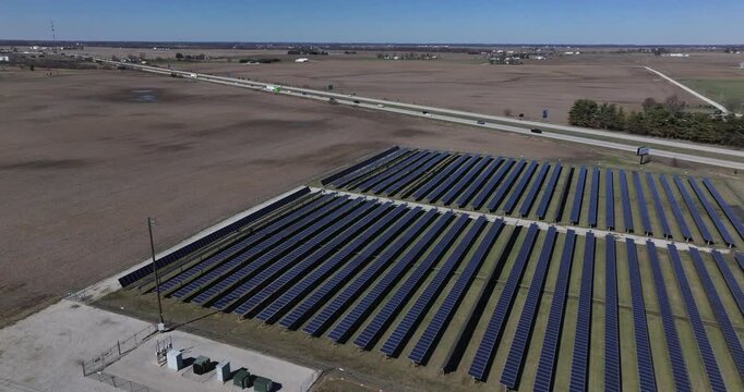 Aerial view of rows of solar panels contrasting with the brown fields beside a busy highway under a clear blue sky, Batesville, Indiana, United States.