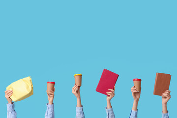 Female hands with books, bag and paper cups of coffee on blue background
