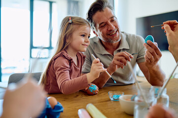 Happy father and daughter enjoying creative bonding painting colorful Easter eggs at home,...