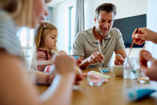 Family members painting Easter eggs with colorful dyes, celebrating a holiday tradition and sharing creative bonding time indoors