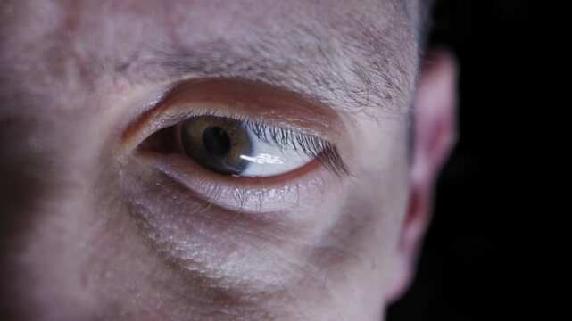 An extreme close-up shot of a human male eye darting nervously and looking around in a dark room. Concept of fear, paranoia, surveillance, intense focus, and human vision.