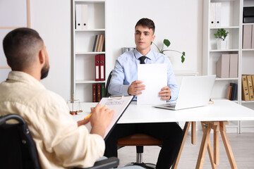 Young lawyer with papers and client in wheelchair working at office