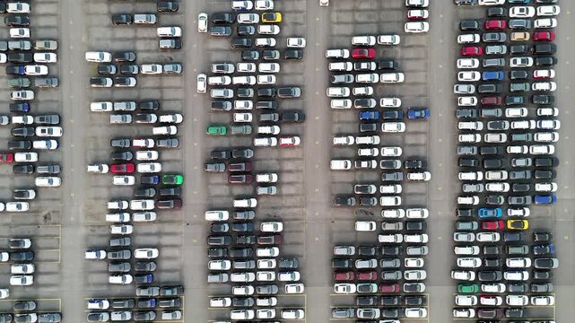 Drone looks straight down on repeating car blocks parking lines and fully occupied automotive storage lots.