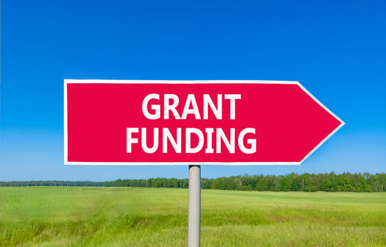 Grant funding symbol. Concept words Grant funding on beautiful red road sign. Beautiful blue sky green grass field background. Business and grant funding concept. Copy space.