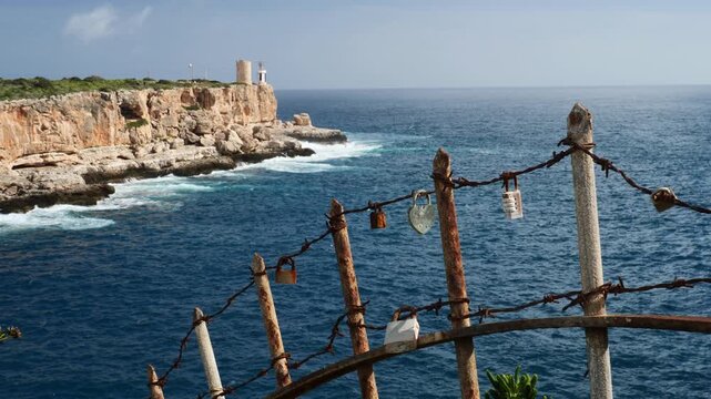Close up of love locks with waves crashing in the rocks in the background. Slow motion x0,5. Cala Figuera, Mallorca, Spain.