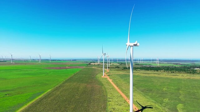 Aerial view of modern wind turbines standing tall amongst lush green fields, generating clean energy under a clear sky, Jeffreys Bay, Eastern Cape, South Africa.
