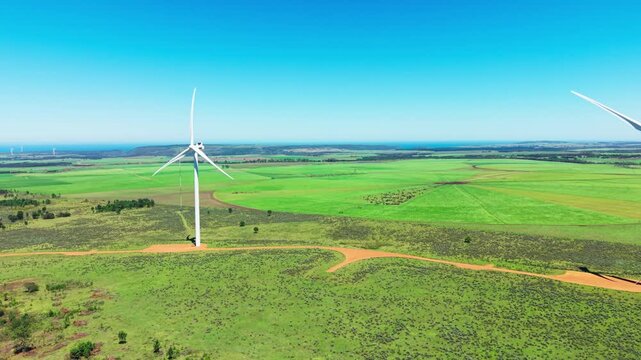 Aerial view of wind turbines standing tall amidst a vibrant green field, blending with the horizon under a clear sky, Jeffreys Bay, Eastern Cape, South Africa.