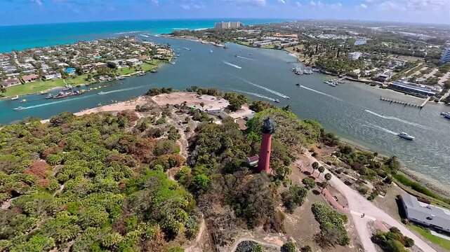 Aerial view of the red Jupiter Inlet Lighthouse surrounded by lush greenery, contrasting with the blue inlet waters, Jupiter, Florida, United States.