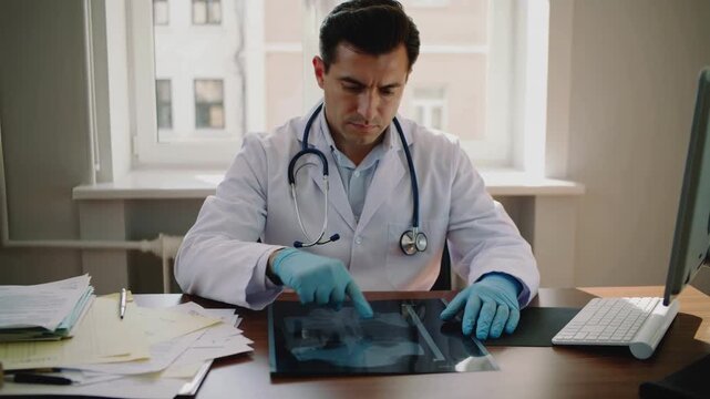 Doctor reviewing X-ray scan at desk during medical consultation in clinic office.