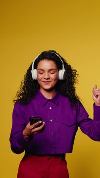 Young woman listening to music with headphones on phone and dancing