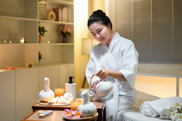 Fototapeta premium Beautiful young woman in white robe relaxing after spa procedures in oriental spa resort, drinking tea. Elegant woman relaxing, finding inner peace and balance