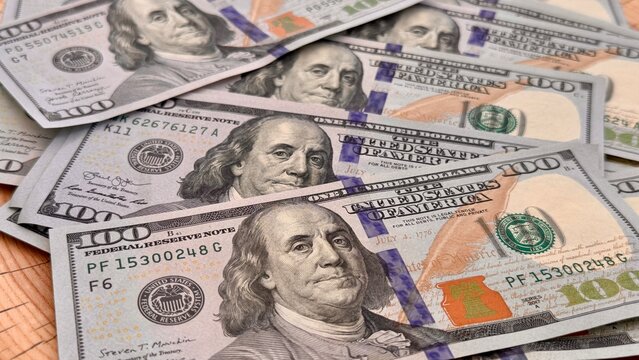 Fan of US hundred dollar bills on a natural cracked tree stump. Money and nature concept, financial growth and environmental investment. Cash currency on rustic wooden background outdoors.