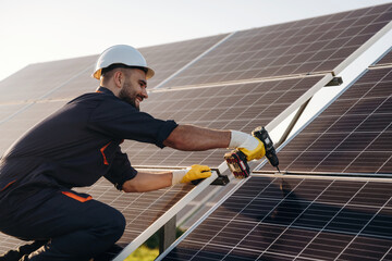Yellow drill is in hands, installation process. Male solar engineer examining photovoltaic panels at a power station