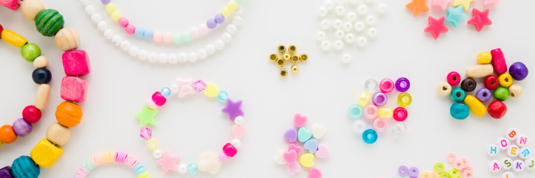 Bracelet, necklaces and colorful different plastic parts on light gray table background. Closeup. Creating beaded jewellery for little child girl. Wide banner. Flat lay. Top down view.