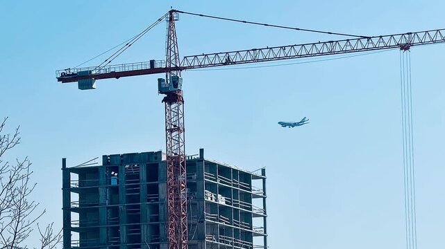 Luxury residential complex construction in an integrated district. Modern apartment buildings, a tower crane, and a cargo plane flying in the blue sky. Urban growth and logistics concept.