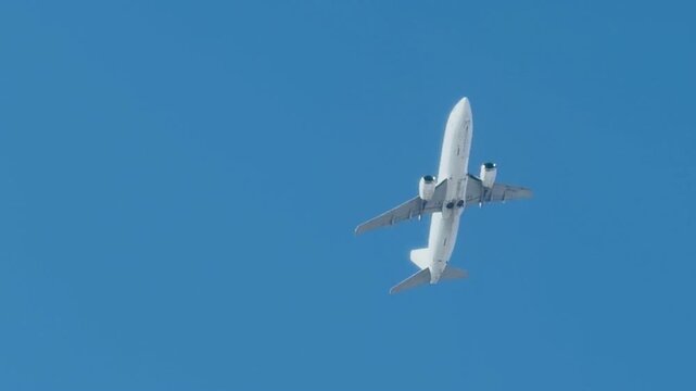 White commercial passenger airplane flying high in the clear blue sky. Modern jet aircraft in flight, bottom view. Concept of air travel, international aviation and global logistics.
