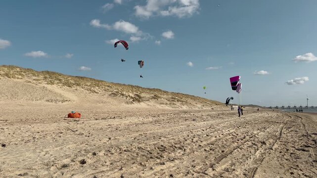 Westenschouwen, Zeeland, Netherlands - March 15, 2026: Wide beach landscape of paragliders with colorful parachute wings flying above sand with equipment on shore, participants and spectators visible.