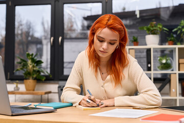 Creative young woman with red hair engaged in work at a modern office space