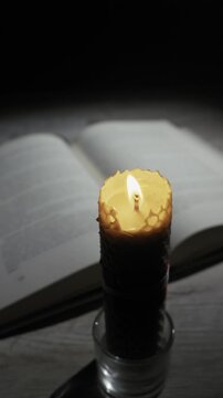 A honeycomb beeswax candle is blown out, releasing smoke in front of an open book in a dark room. Concept of ending prayer, late night study, religious rituals, and extinguishing light.