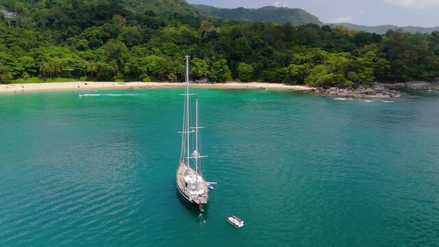 Aerial view of a luxury yacht anchored off Haad Laem Sing beach, Phuket, Thailand. A jet ski races across the clear blue water by the sandy shore