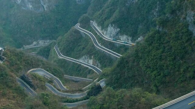 Winding mountain road with sharp hairpin bends carved into steep cliffs in Zhangjiajie, Hunan, China. Travel and tourism landmark. Extreme landscape infrastructure. Vertical orientation