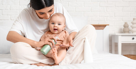Happy mother applying cream on her cute little baby on bed at home