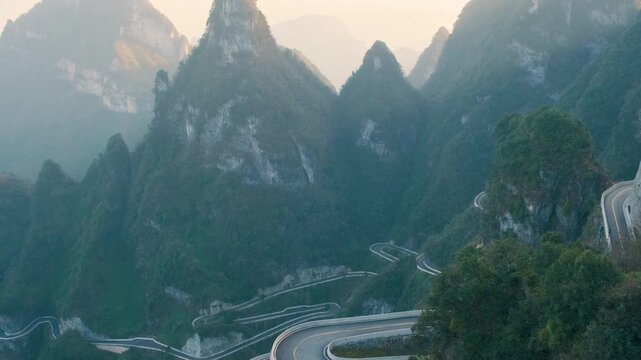 Mountain road landscape of Tianmen Mountain Road with hairpin turns through lush karst peaks and forest valleys at sunrise.in Tianmen Mountain National Park, Zhangjiajie, Hunan, China