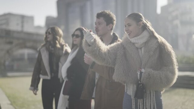 Four young friends stand outside, pointing and reacting with surprise and joy. A group of happy young people are impressed by something unseen in the city.