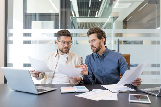 Two business colleagues working together, discussing documents and analyzing data during a corporate meeting in a contemporary office setting, demonstrating teamwork and partnership